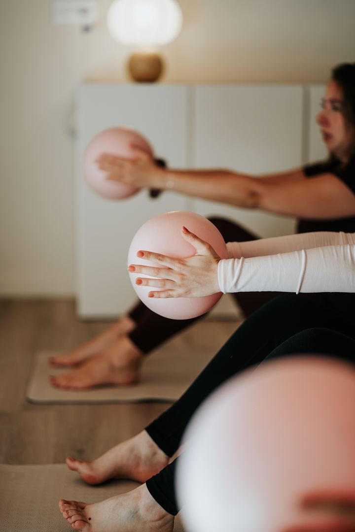 Un cours de Pilates : les mains posées sur de petits ballons roses