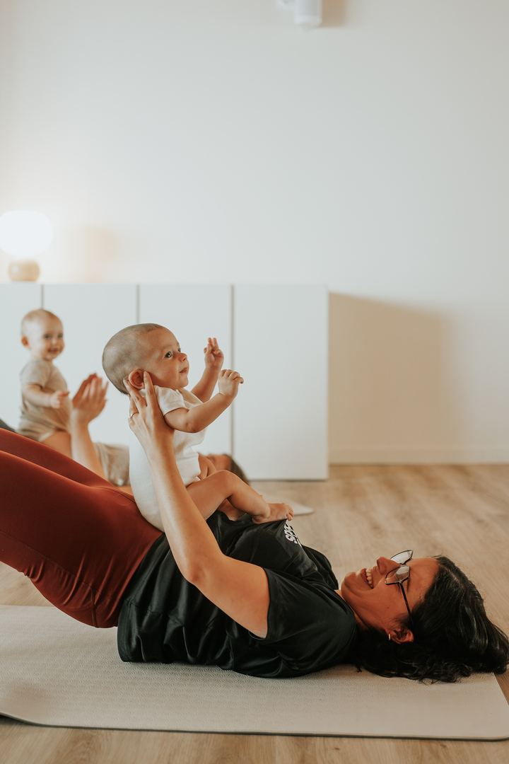 Une maman allongée sur son tapis soulève son bébé en souriant